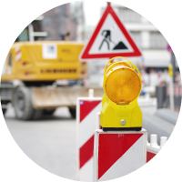 Baustellen-Verkehrsschild und Warnbarken mit einem Bagger im Hintergrund