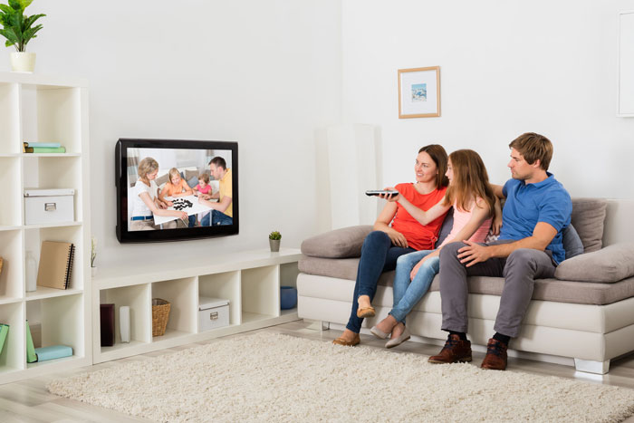 Familie sitzt im Wohnzimmer und sieht TV